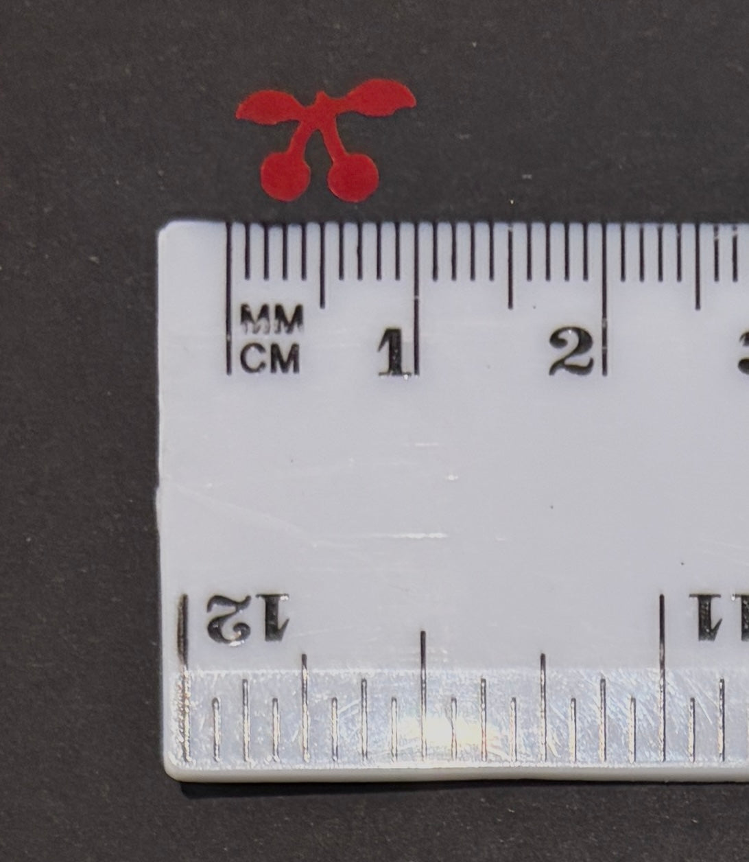 Single red cherry glitter shape confetti next to a white ruler on a black background