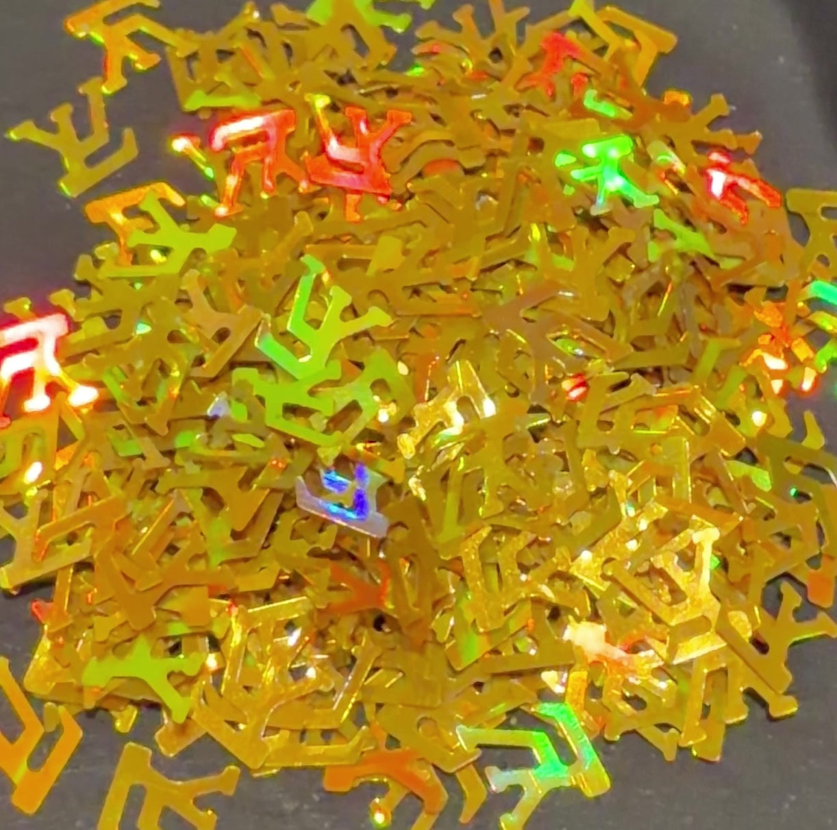 Video of holographic gold LV shaped glitter confetti falling on black background